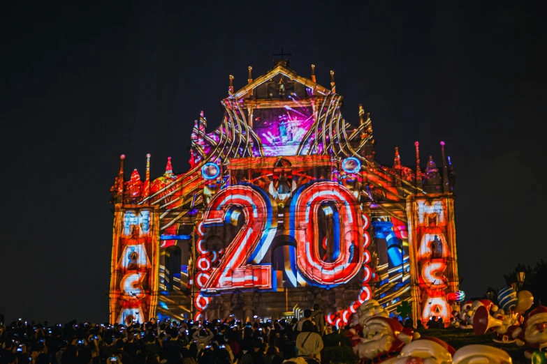 a large crowd watches an illuminated sign display at night