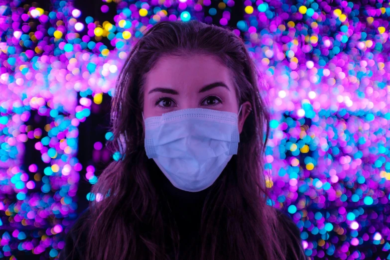 a woman with a medical mask in front of colorful lights