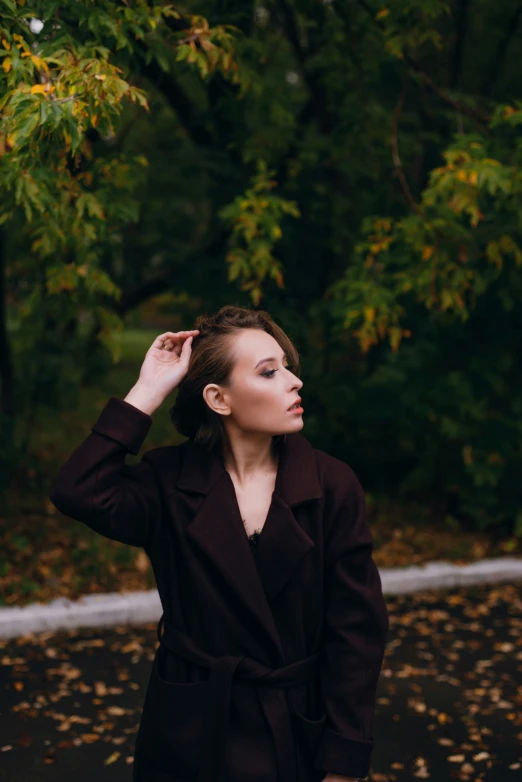 a woman is standing in front of trees wearing a black coat