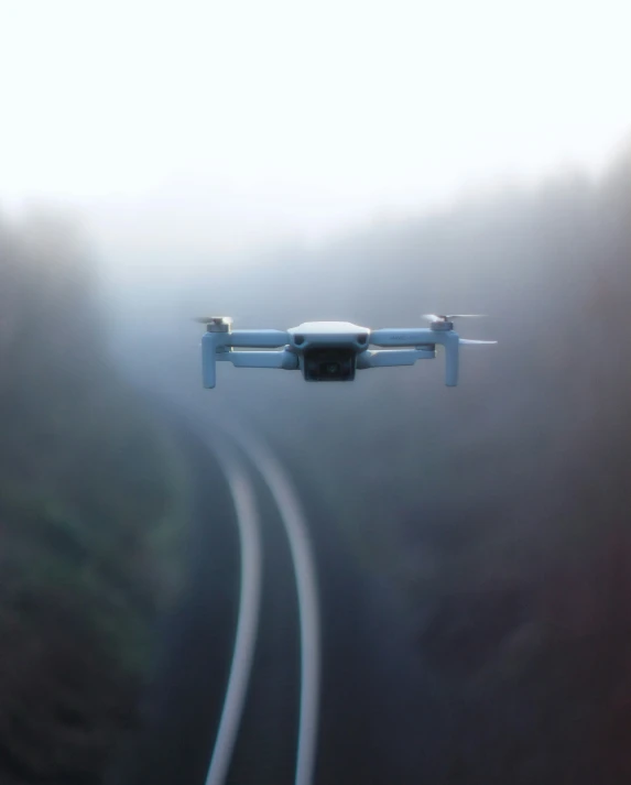 a small grey and white airplane flying over railroad tracks