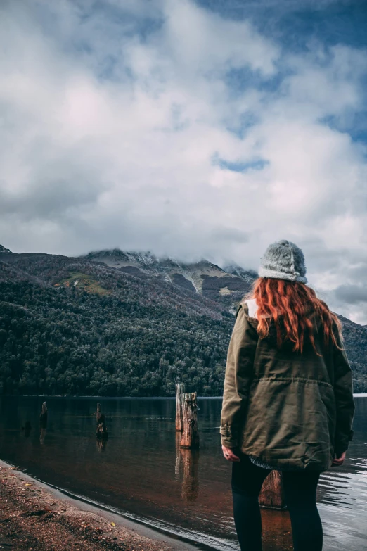 a woman standing next to water in front of mountains