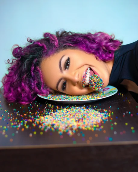 an adorable purple haired woman looking up at her plate of sprinkles