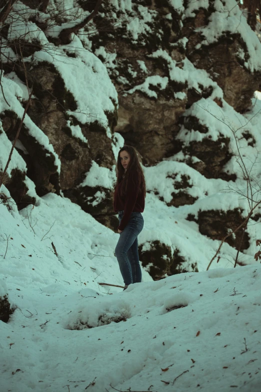 a woman standing in the snow, with snow on her and rocks in the background