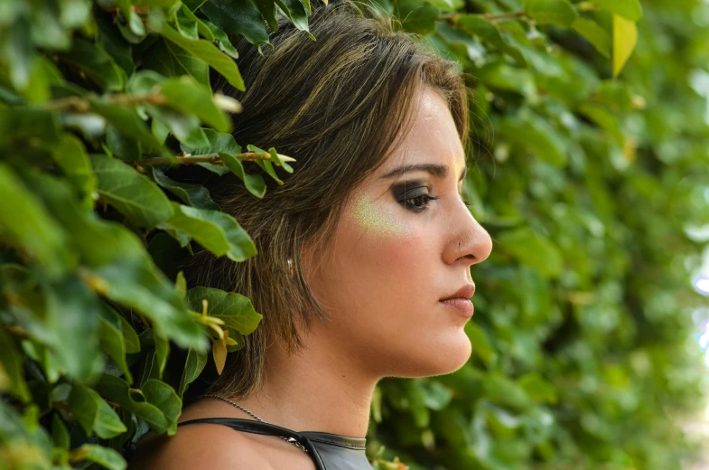 a beautiful young woman standing in front of a hedge