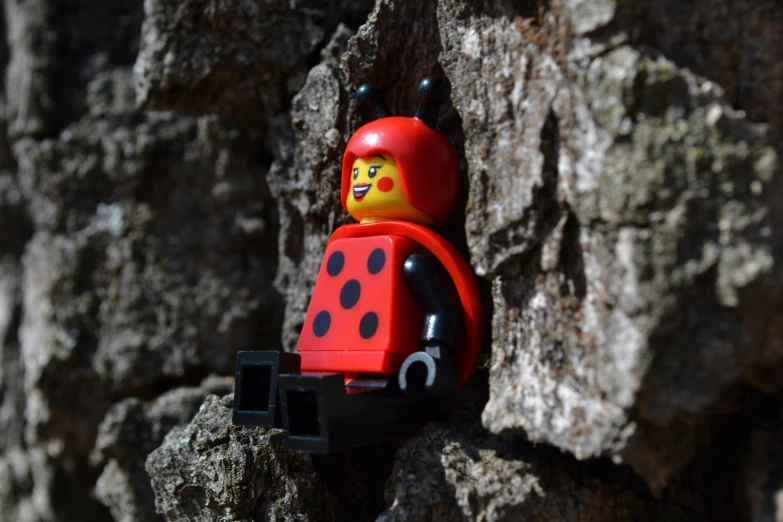 a lego figure wearing a lady bug suit on a stone wall