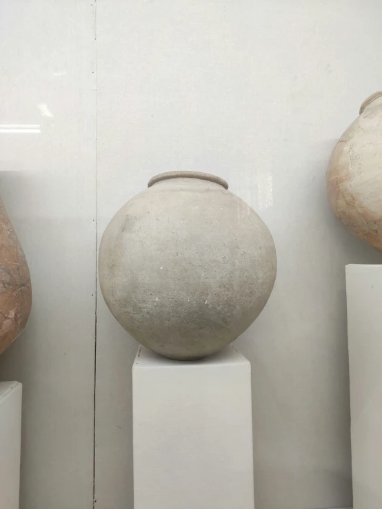 three stone vases and two white pedestals are on display