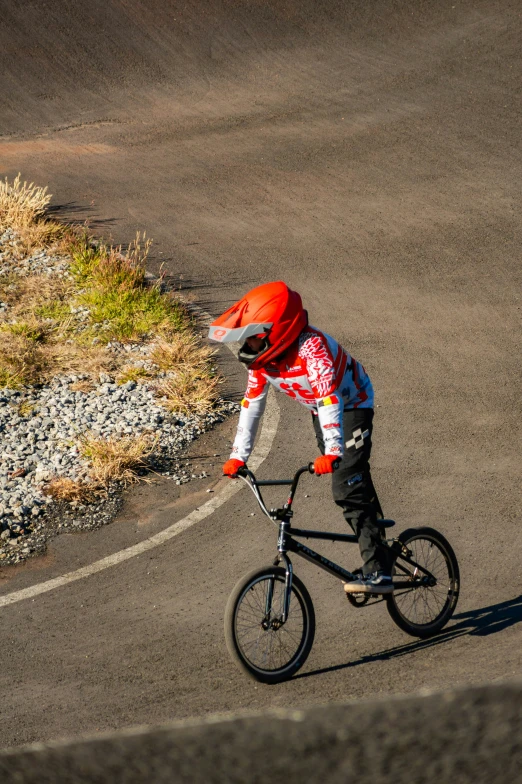 boy in orange helmet on bicycle riding along curved road