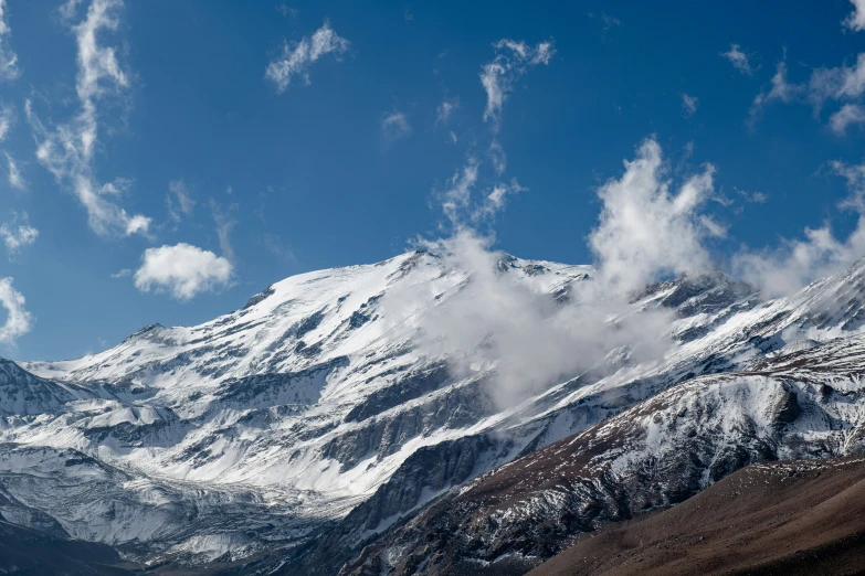 mountain range covered in snow and clouds, with a single skier on top