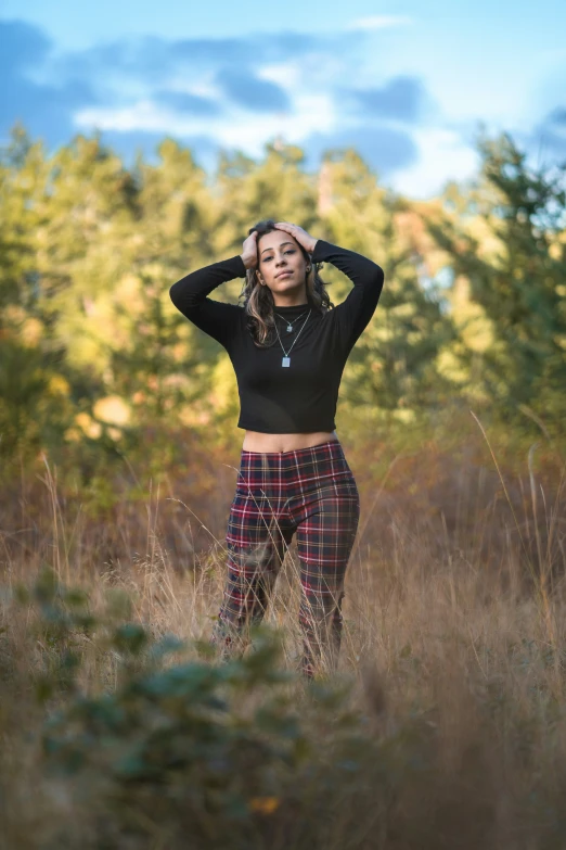 woman with hand on her head wearing plaid pants, standing in field