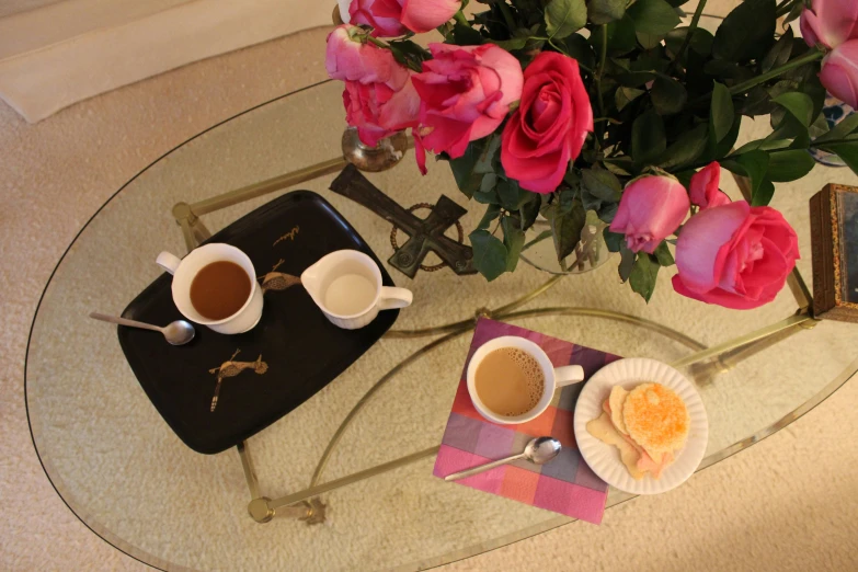 two cups of coffee, two spoons, and a flower on a small table