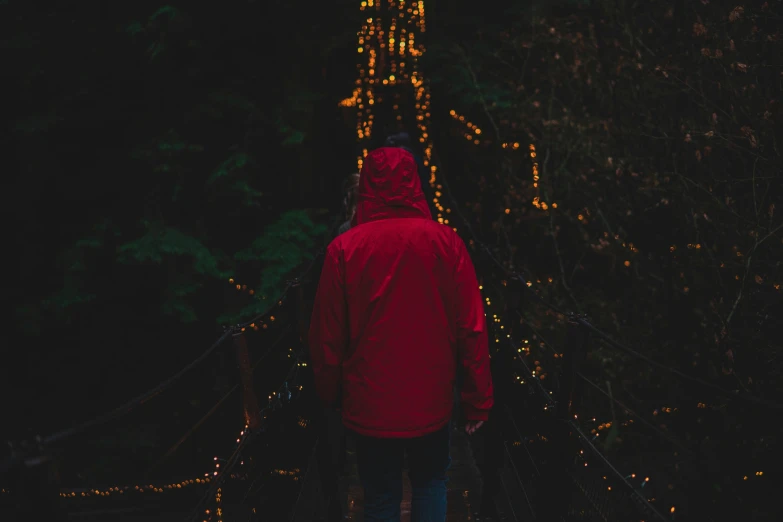 someone in red hoodie standing on suspension bridge at night