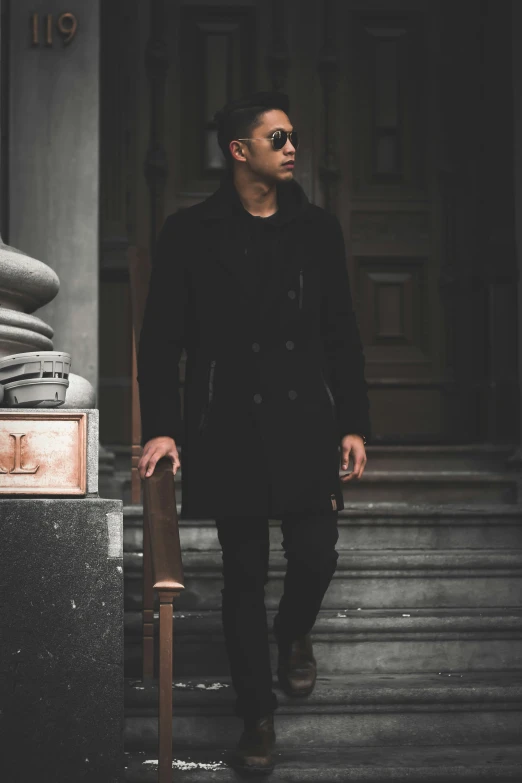 a young man wearing a jacket, shirt and tie and sunglasses is walking up a set of stairs