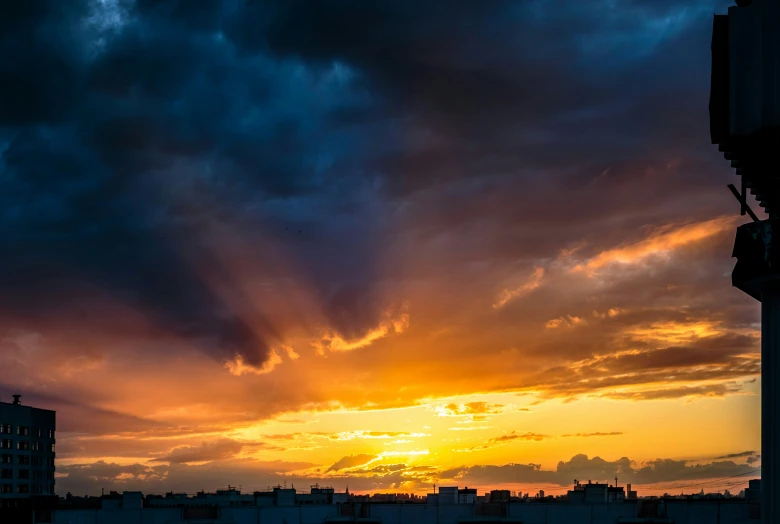 the sun setting on a cloudy day behind a silhouette of buildings