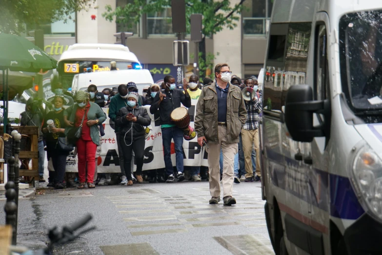 people in masks waiting at an intersection on a street