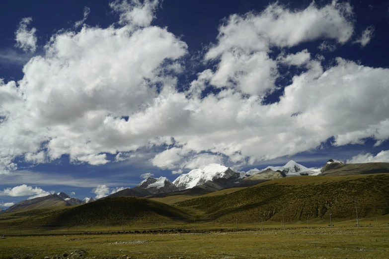 a grassy field surrounded by hills and snow capped mountains