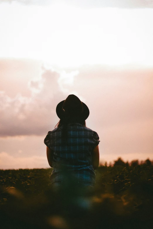 man in hat sitting on field watching sunset