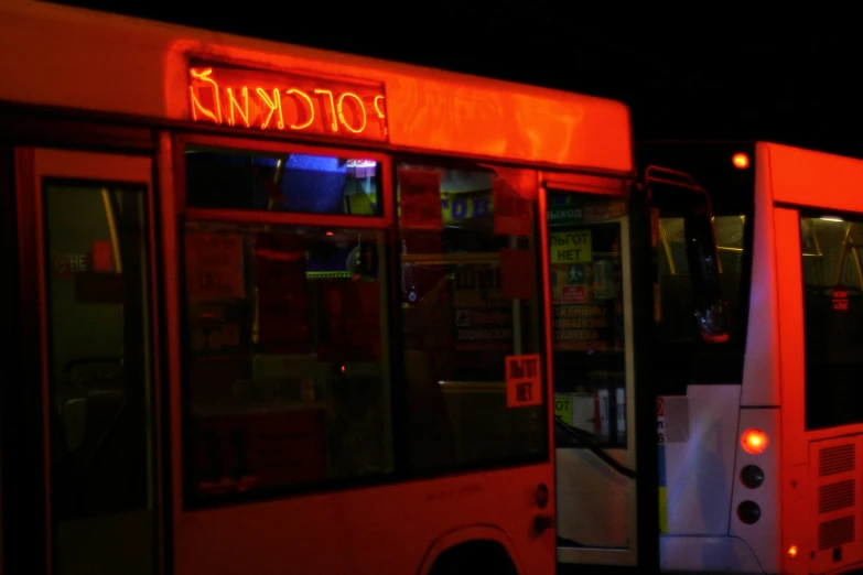 an outdoor restaurant is lit up at night by two red buses