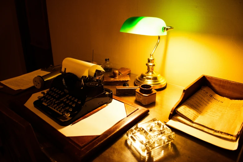 a green lamp, an old typewriter, and other objects on a desk