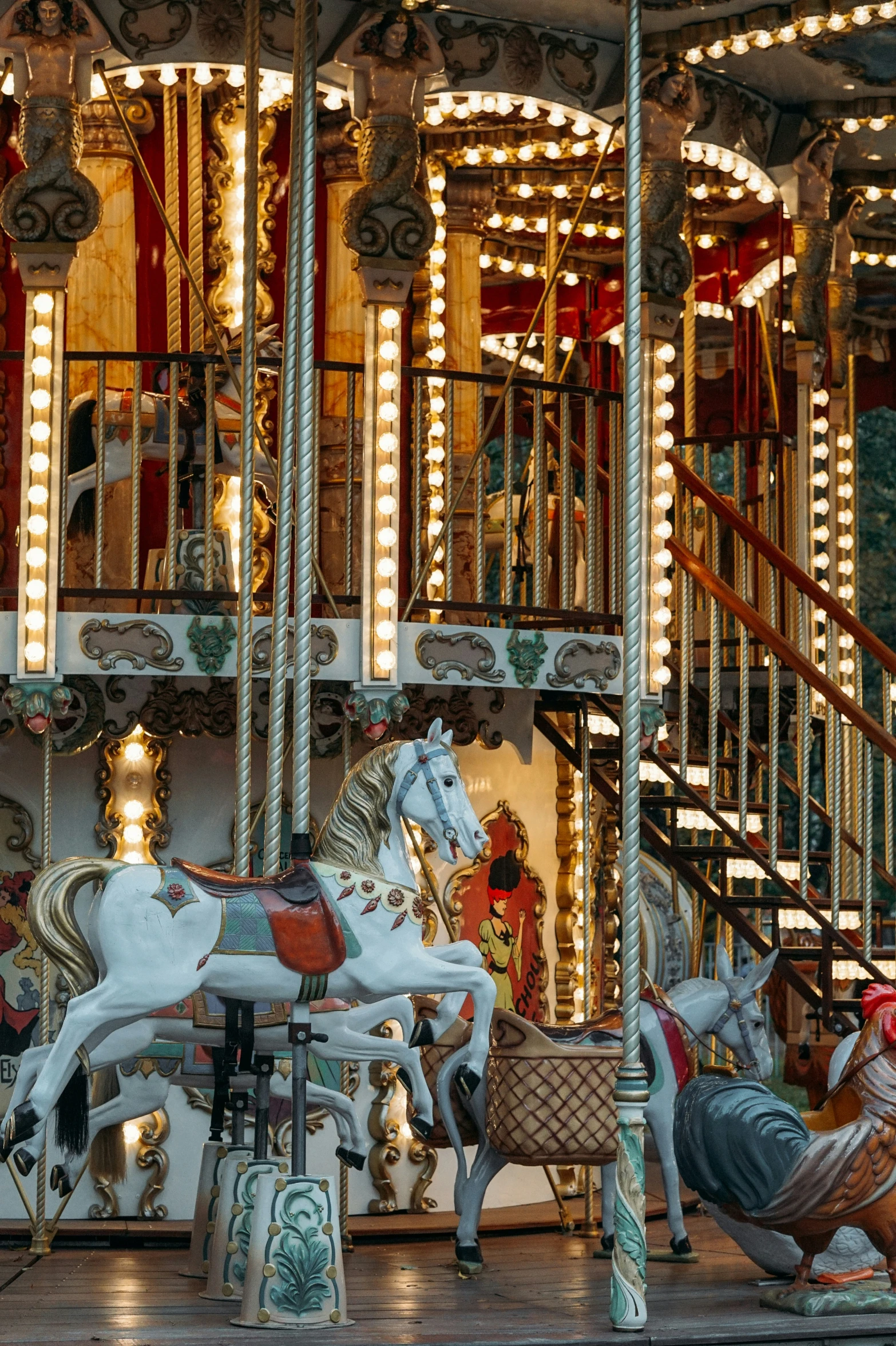 two colorful carousel horses near each other in front of a spiral stair case