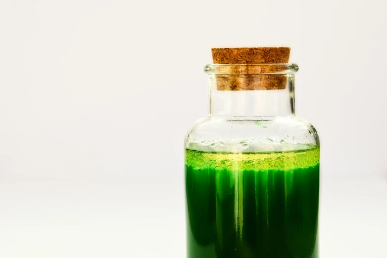 a glass bottle with green liquid inside sitting on a table