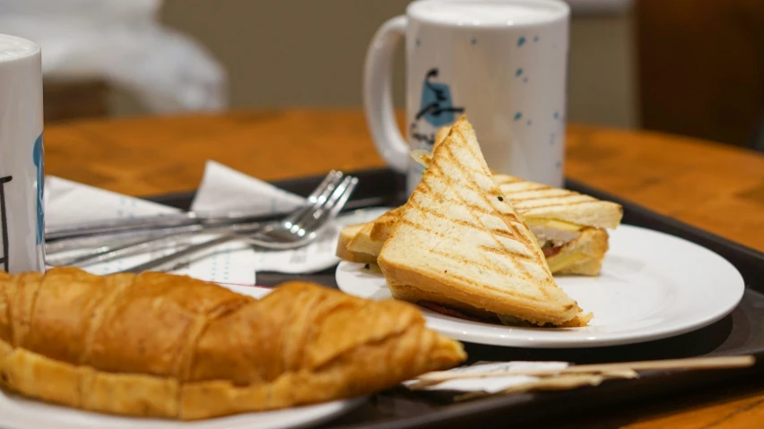 a tray with toast, croissant and coffee on it