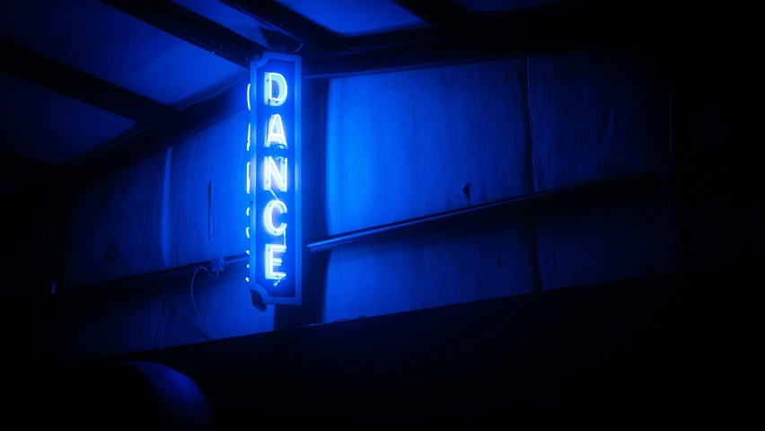 there is a neon dance sign hanging from the side of the wall