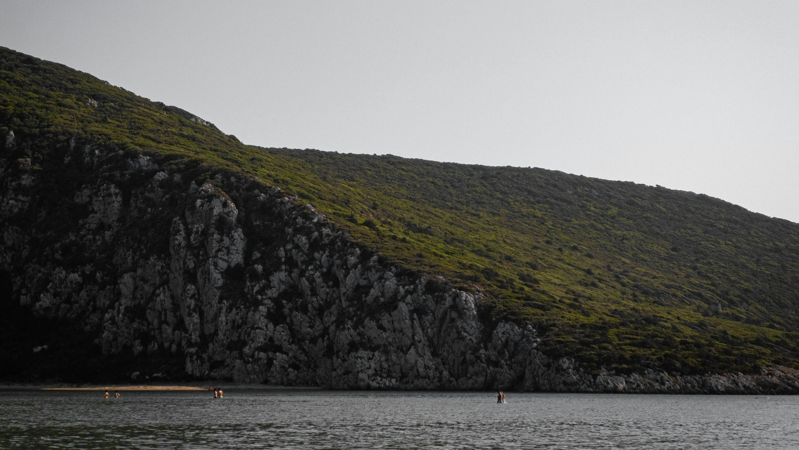 two men walking on the beach near a rocky cliff