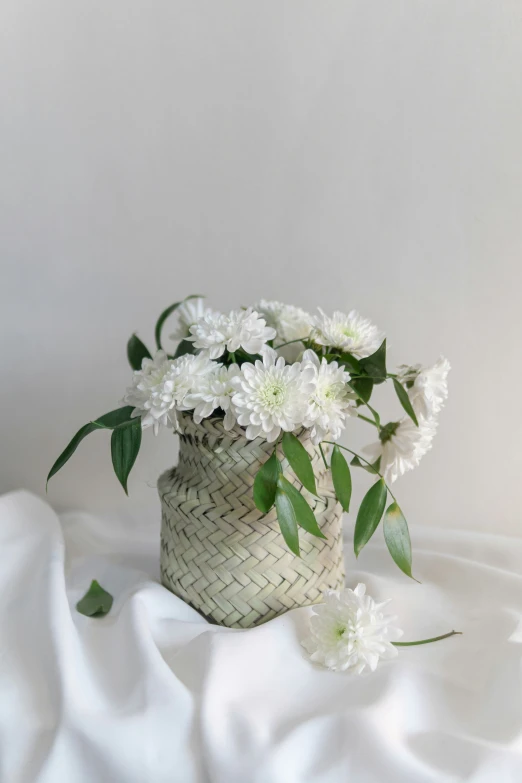 a basket of white flowers on a bed with a white cloth