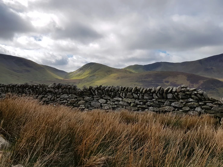 a field with a stone wall next to grass and mountains