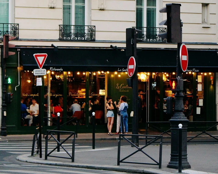 a view of a corner of a street, with people standing outside and enjoying the night