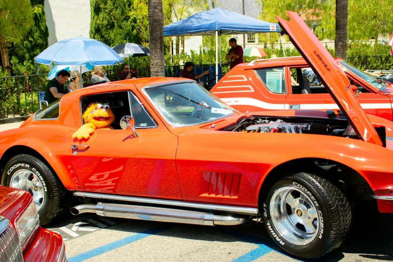 an orange car with its hood open parked next to another car