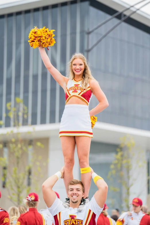 two cheerleaders are standing atop each other and the cheerleader in uniform holds a pom pom above their head