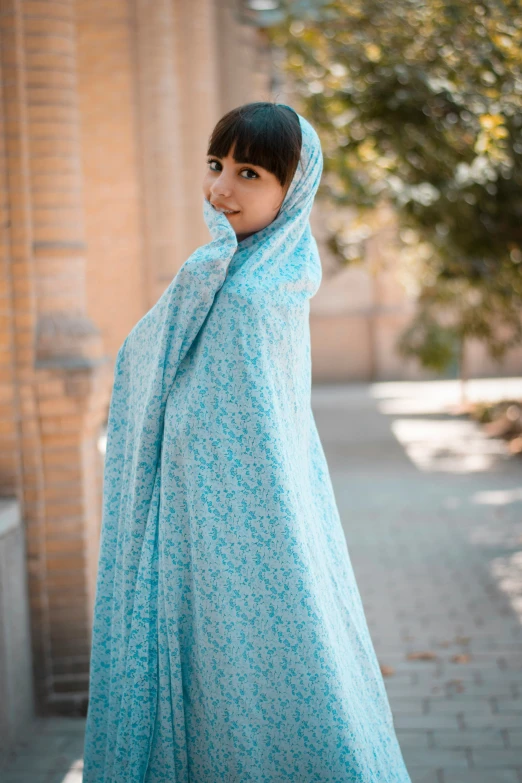 a woman wearing a blue scarf stands near a building