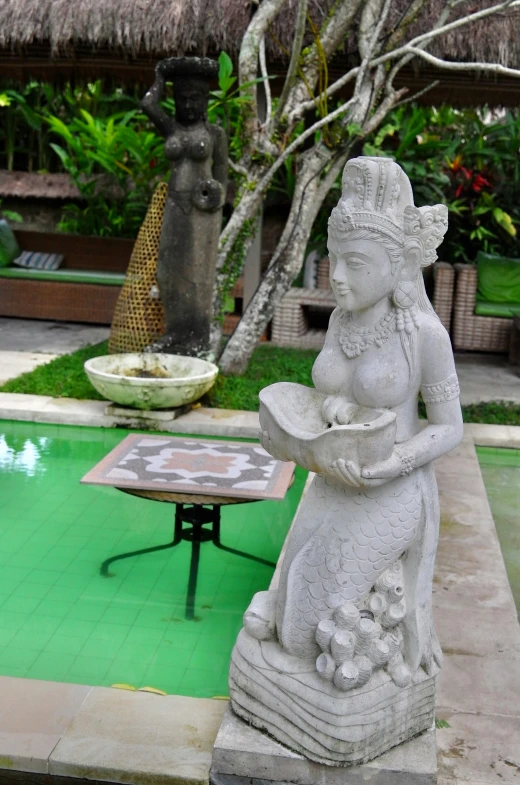 a statue stands in front of a pool surrounded by flowers and potted plants