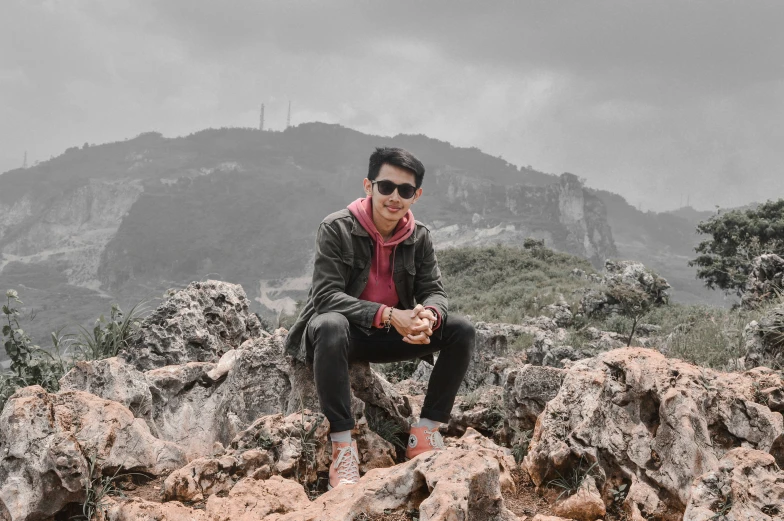 a man sitting on top of rocks with the mountains in the background