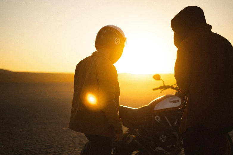 two men are near a motorcycle at sunset