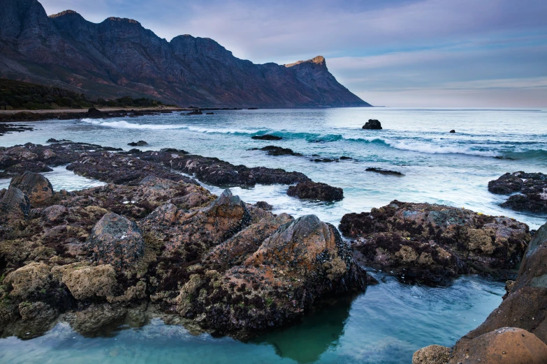 a rocky coastline is near the ocean and mountain tops