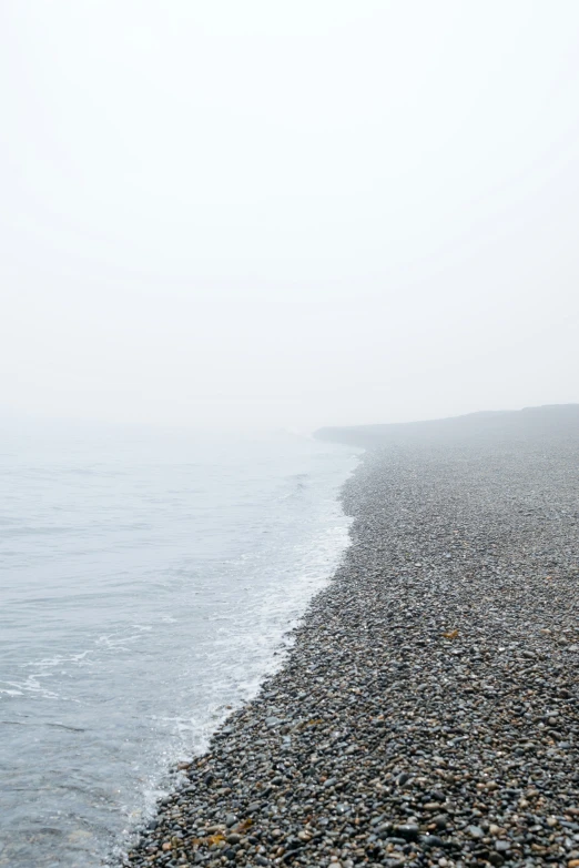 a wet beach lined with pebbles on a foggy day