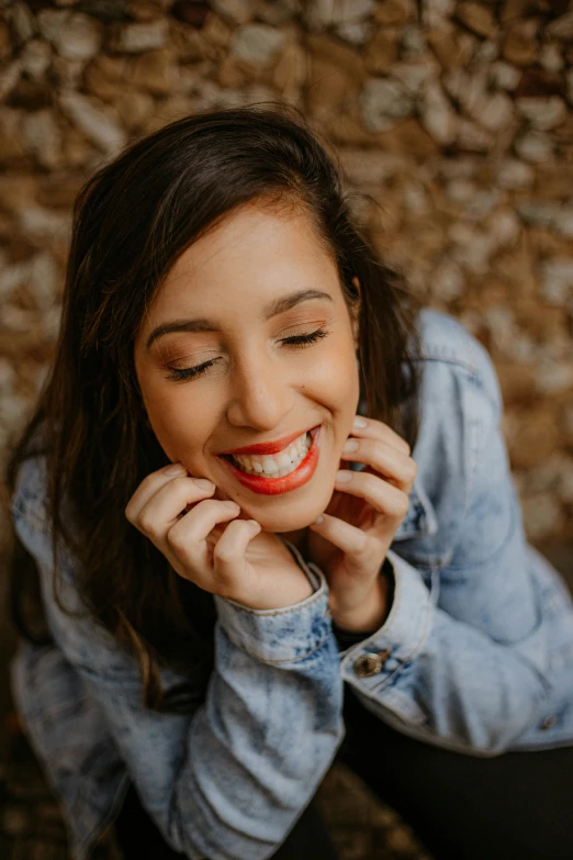 the woman smiles while sitting down and holding her hands to her face