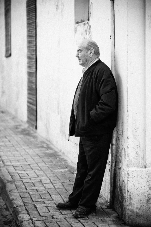 an old man leaning against a wall in a suit