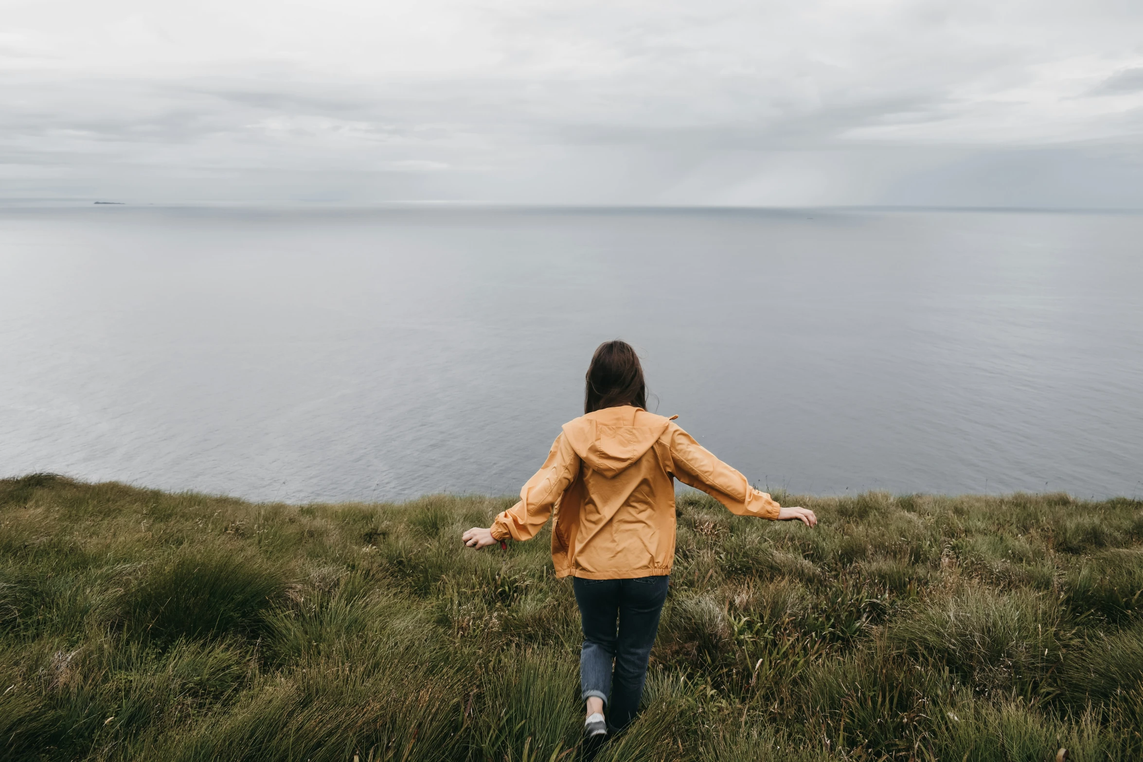 a woman stands alone on a hill facing the water