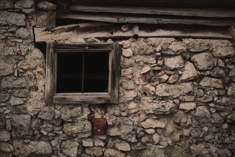 a dirty stone wall that has a barred window