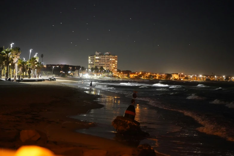 the shore line of the beach at night with some buildings