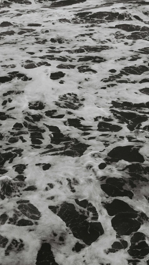 an ocean beach with dark, rocky rocks and white foam