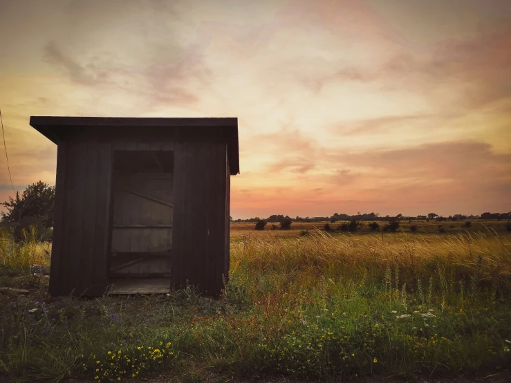 a outhouse in a grassy field at sunset