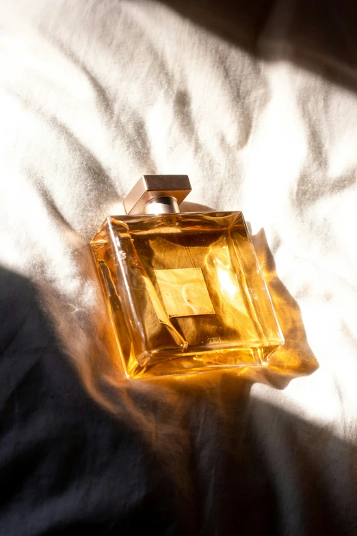 an empty yellow square perfume bottle on a bed