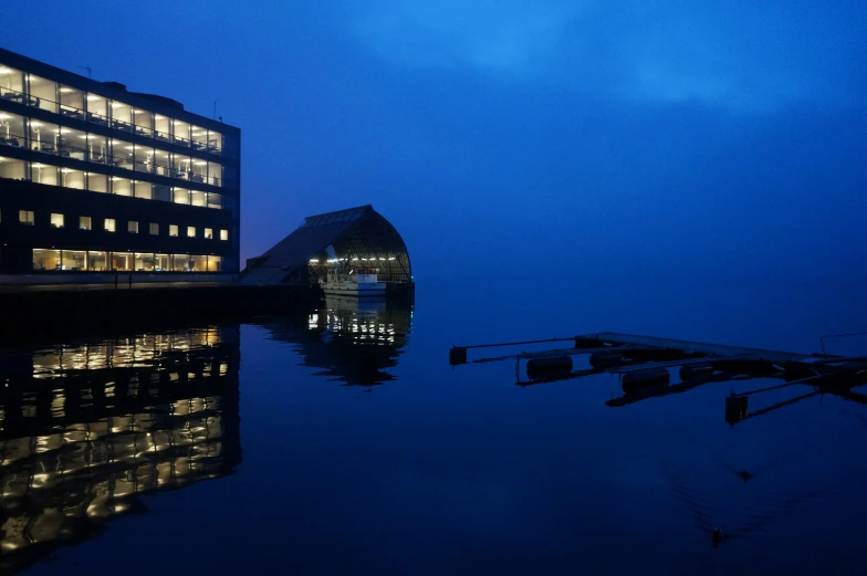 the water in front of a building with lights on it and a boat on the side