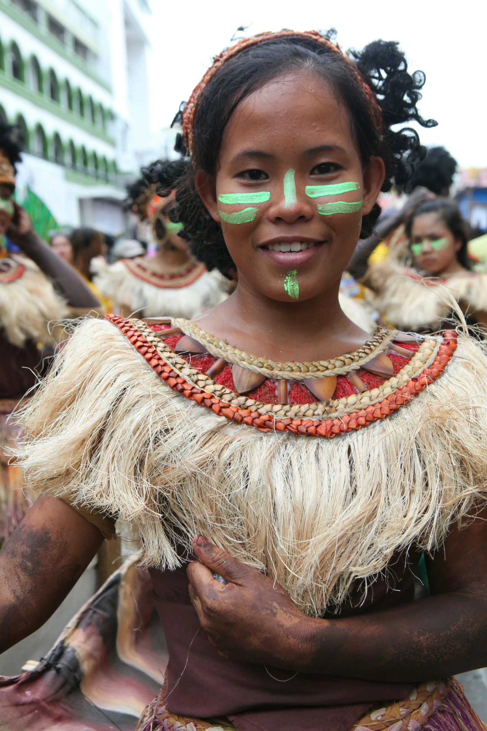 a child with painted face paint, holds on to her arms and stands in a crowd