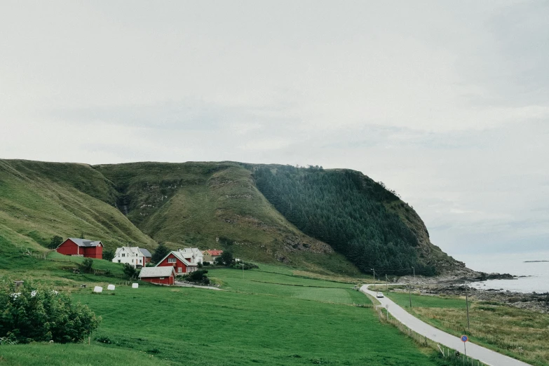 there is a red house sitting on the grass by a hill