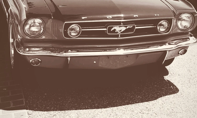 an old mustang mustang sits in the shade with its headlight turned on